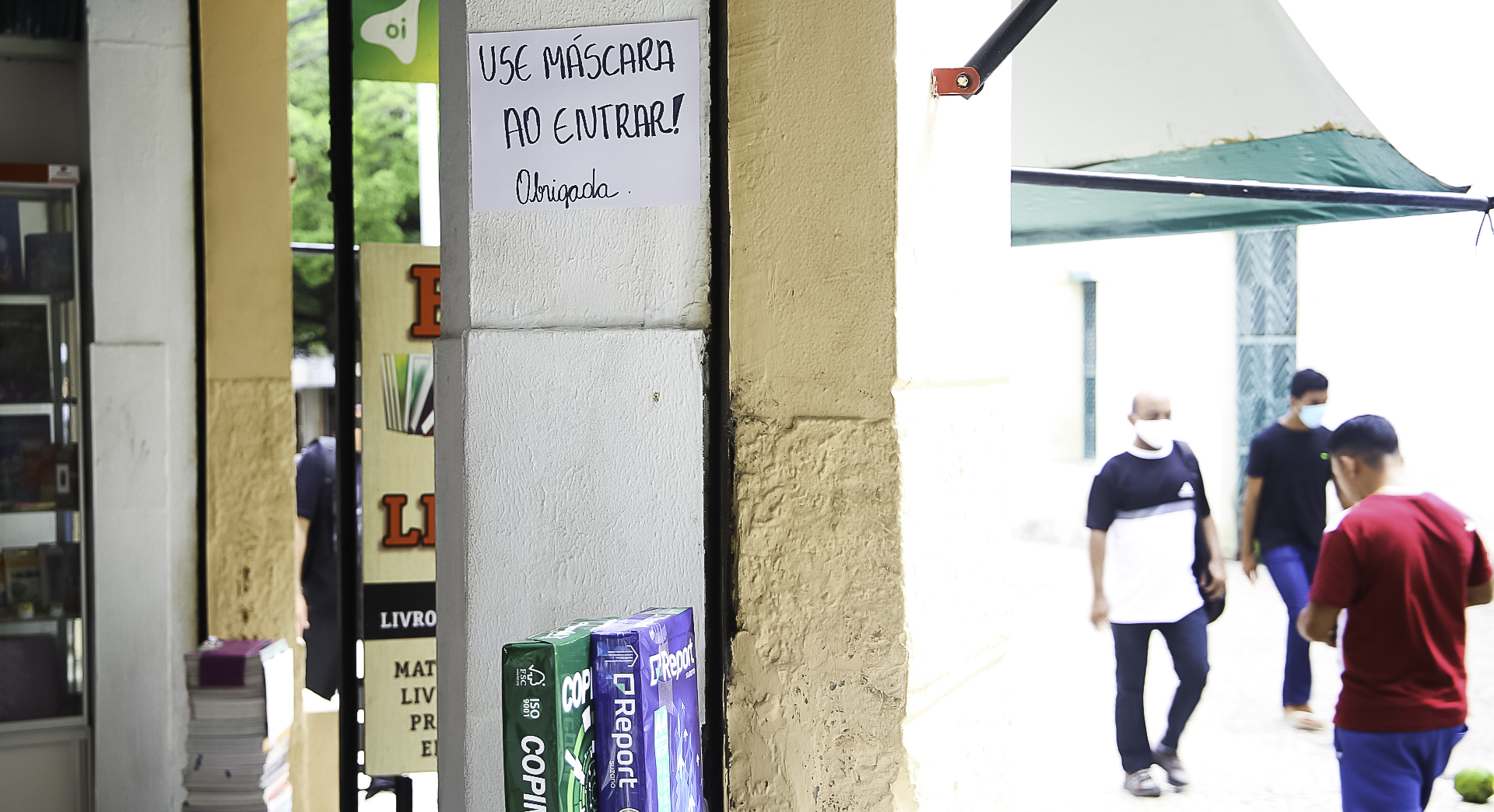 a foto mostra o detalher do interior de uma loja no centro com um cartaz escrito à mão com a frase use a máscara ao entrar